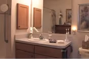 Bathroom vanity with a sink, mirror, medicine cabinets, toiletries, and a shower curtain and framed art visible in the background.