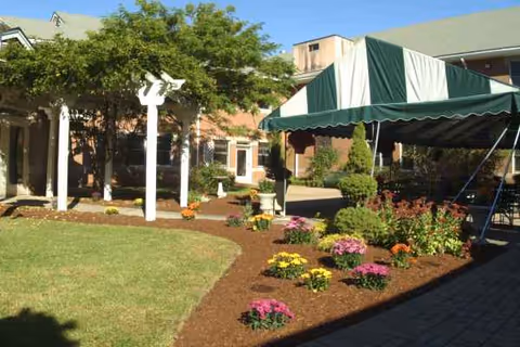 Exterior view of Southwood at Norwell Nursing showing garden beds and a striped canopy.