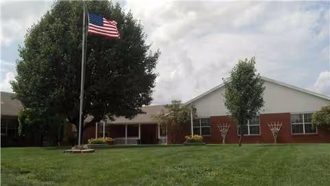 Exterior view of Hartville Care Center with flagpole, trees, and a brick front.