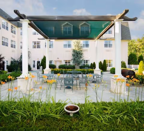 Outdoor courtyard with metal tables and chairs under a shaded pergola near a residential building.