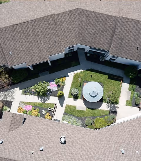 Aerial view of a landscaped courtyard with a central gazebo, walkways, flower beds, and surrounding building roofs.