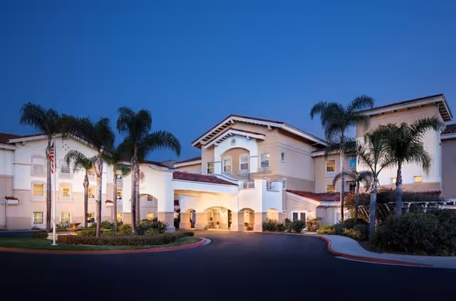 Front exterior view of Belmont Village Senior Living Sabre Springs with palm trees at dusk.