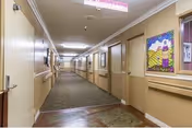 Long interior hallway of a senior living facility with doors on both sides, handrails, overhead lights and framed artwork on the walls.
