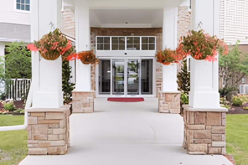 Covered entrance with stone pillars and hanging flower baskets leading to glass doors.