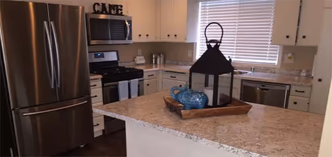 Modern kitchen with a center island topped with a decorative lantern and tray, stainless steel refrigerator, stove, microwave, dishwasher, and white cabinets.