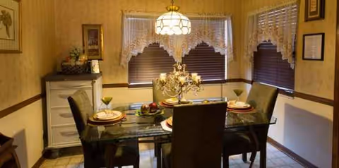 Cozy dining room with a glass-top table, cushioned chairs, and a chandelier.