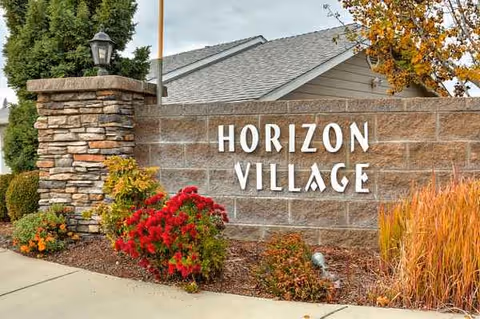 Stone sign reading Horizon Village at the entrance with landscaping and a building in the background.