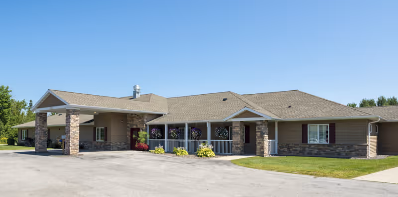 Front exterior of a single-story senior living building with a covered entrance, stone accents, and a driveway.