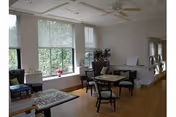 Bright common lounge with tables, chairs, large windows, and indoor plants.