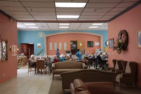 Residents seated at tables in a communal dining and activity room with a lounge seating area in the foreground.