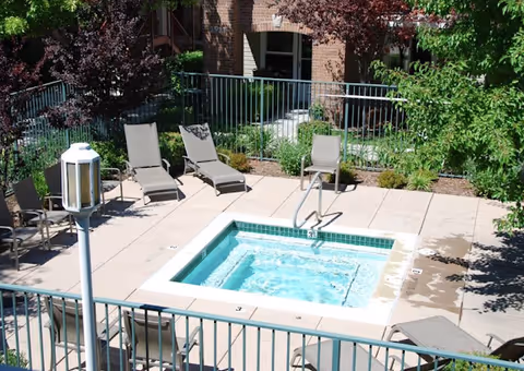 Small outdoor hot tub in an apartment courtyard surrounded by lounge chairs, plants, and a metal fence.