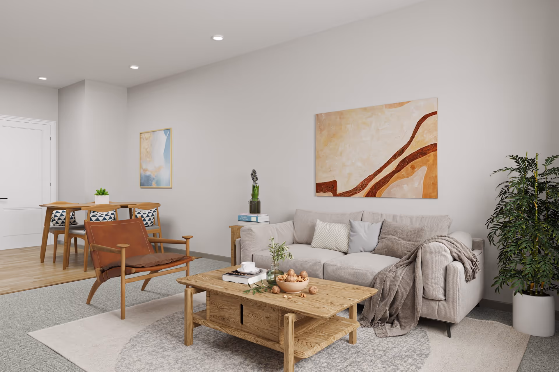 A modern living room with a beige sofa adorned with multiple cushions and a throw blanket, a wooden coffee table with a bowl of nuts, books, and a cup, a brown leather armchair, a large potted plant, and abstract artwork on the walls. In the background, there is a wooden dining table with four chairs and a small plant centerpiece.