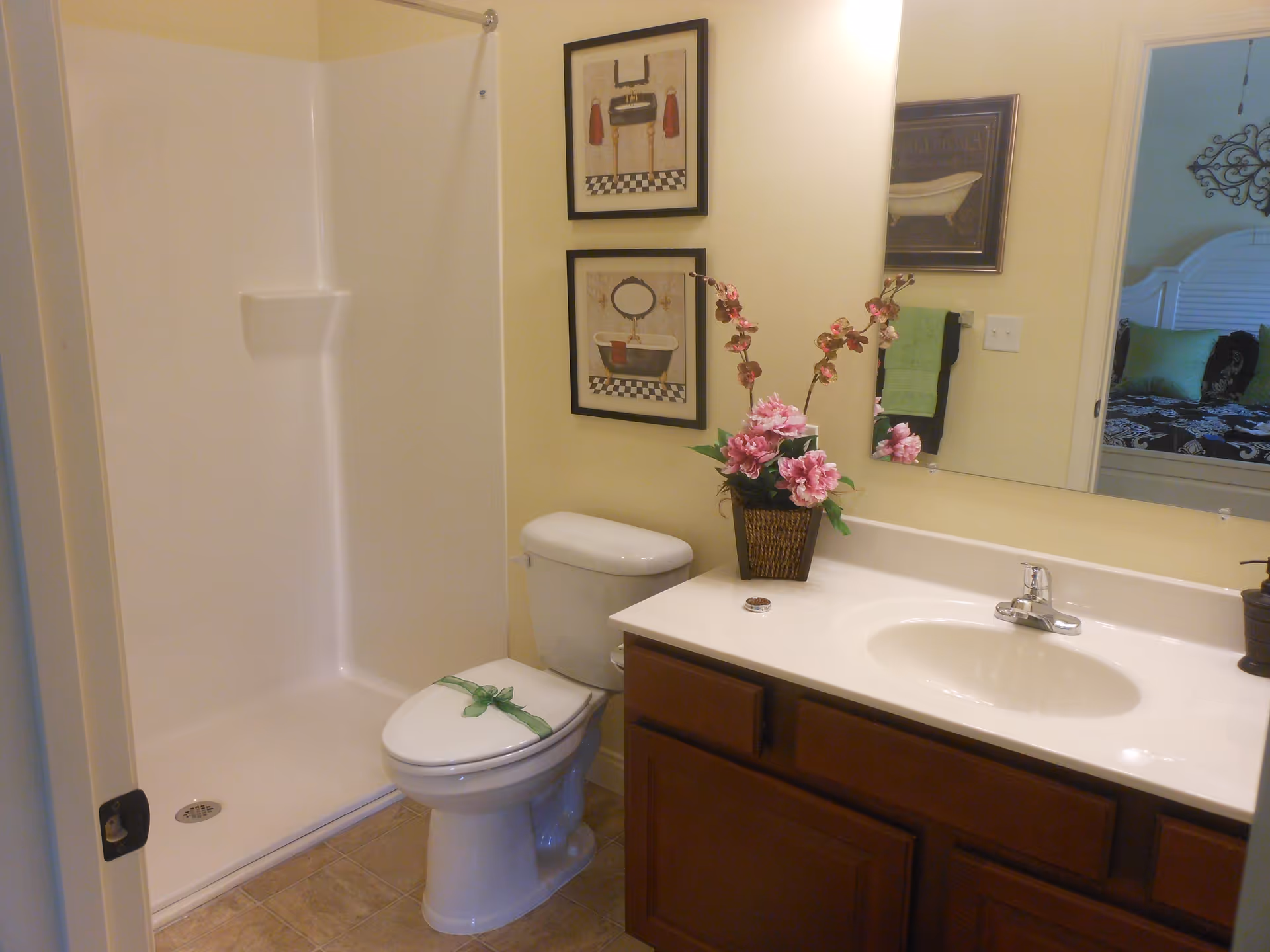 Bathroom with a shower stall, toilet, vanity sink, mirror, framed art and a vase of pink flowers on the counter.