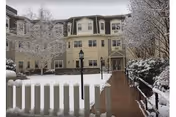 Snow-covered senior living building with a white picket fence and lamppost at the entrance.