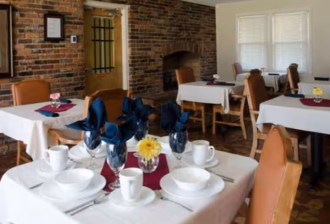 Dining room with white tablecloths, navy napkins, and a brick wall.