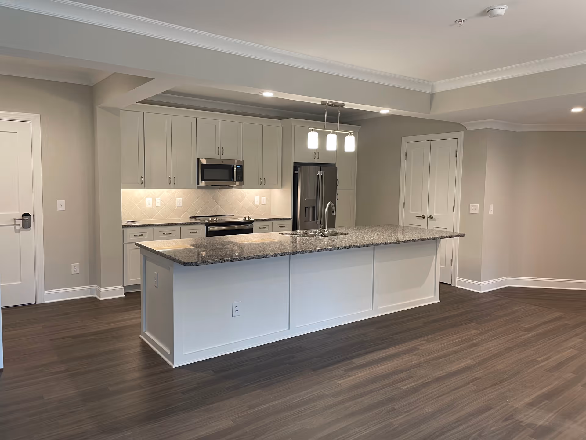 Open modern kitchen with a large island, granite countertop, white cabinets, stainless steel appliances, and wood-look flooring.