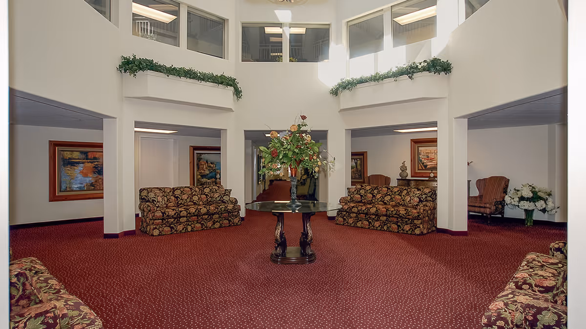 Two-story open lobby with red patterned carpet, floral-upholstered sofas and a central round table topped with a large floral arrangement.