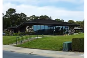 Exterior view of a single-story senior living facility with glass walls, ramp, and lawn.