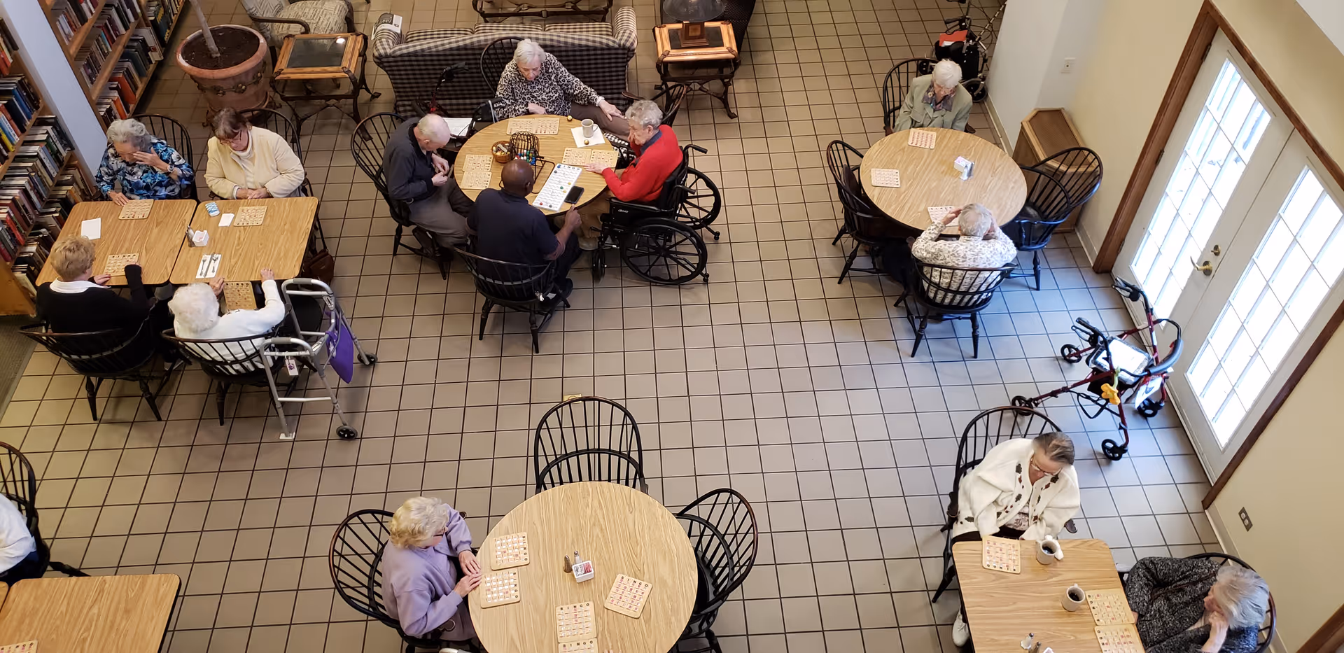 Overhead view of seniors seated at round tables in a communal activity room playing bingo.