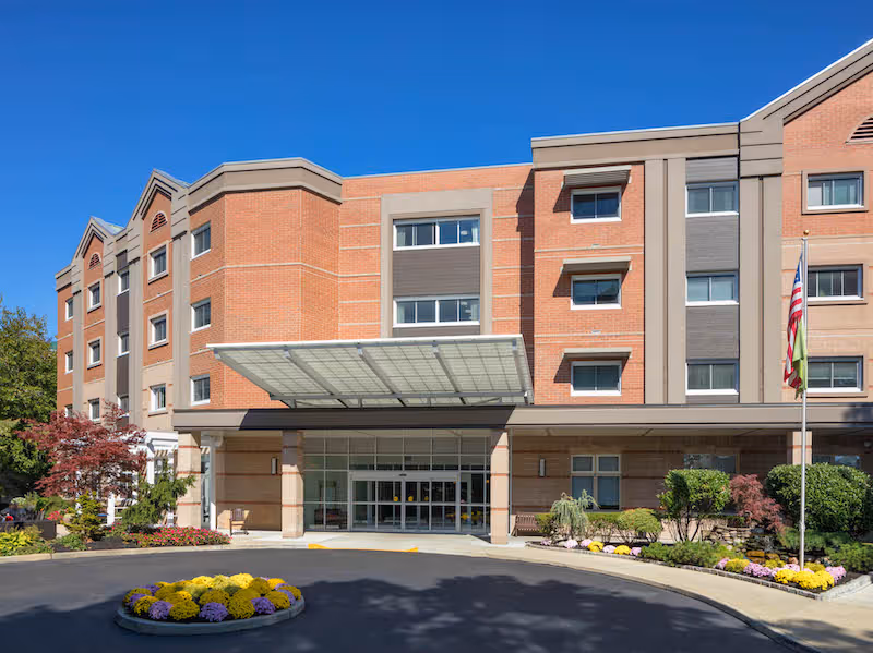 Front exterior of Atria Park of Lynbrook, a brick senior living building with glass entrance.