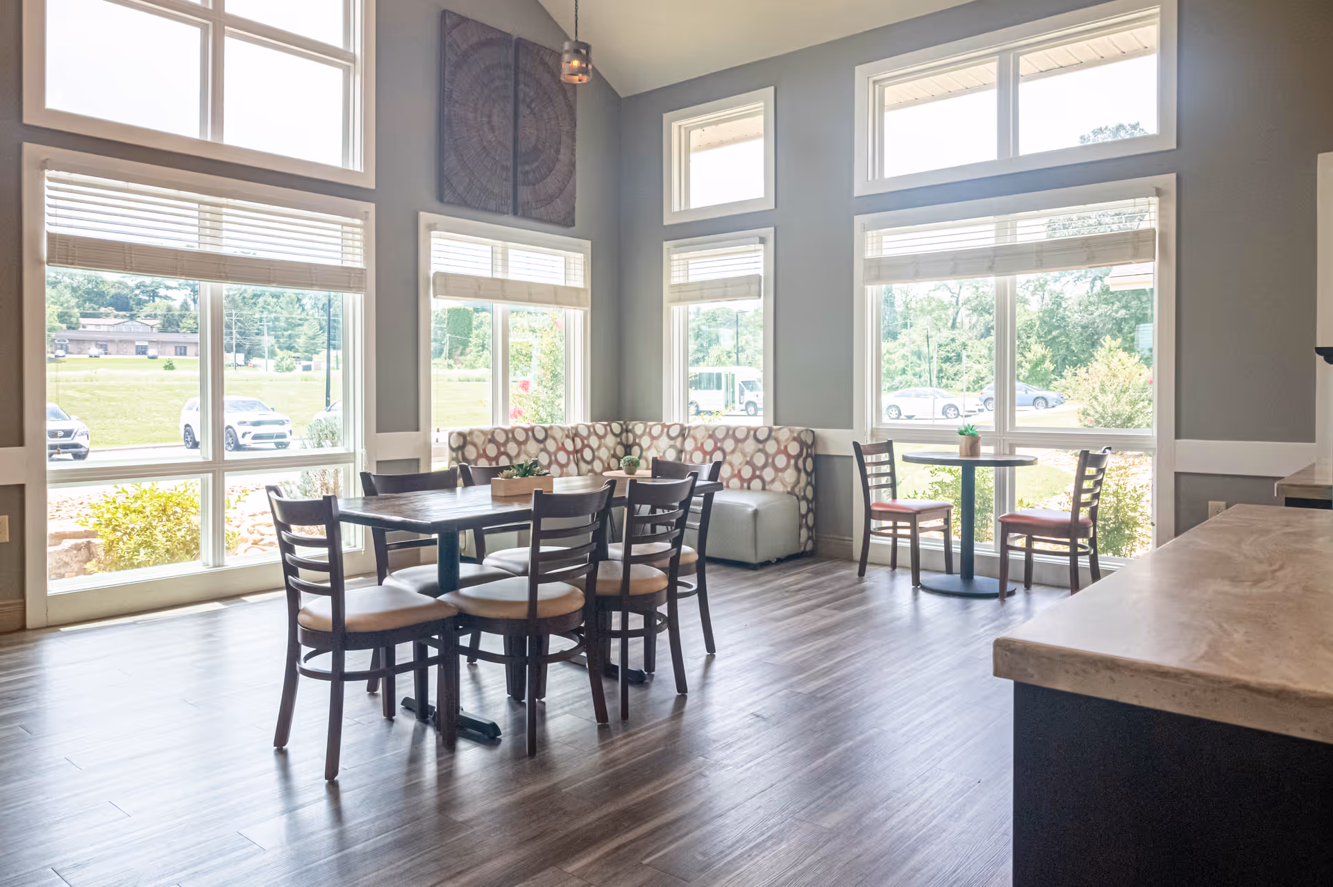 Bright common dining area with tables, chairs, booth seating and large windows.