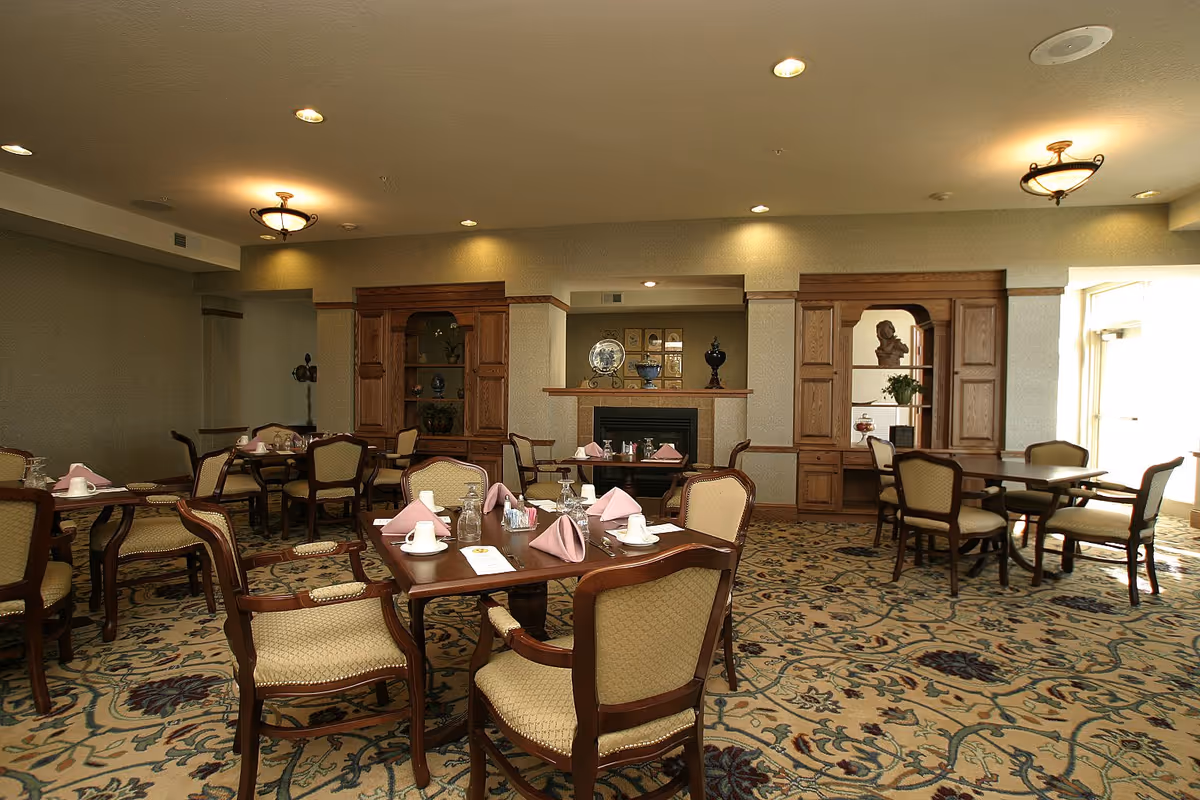 Dining room with several tables set with napkins and cups, upholstered chairs, and wooden cabinetry along the back wall.