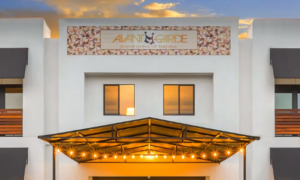 Exterior front view of AvantGarde Senior Living of Tarzana building at sunset, featuring a white facade with two windows and a covered entrance with string lights.