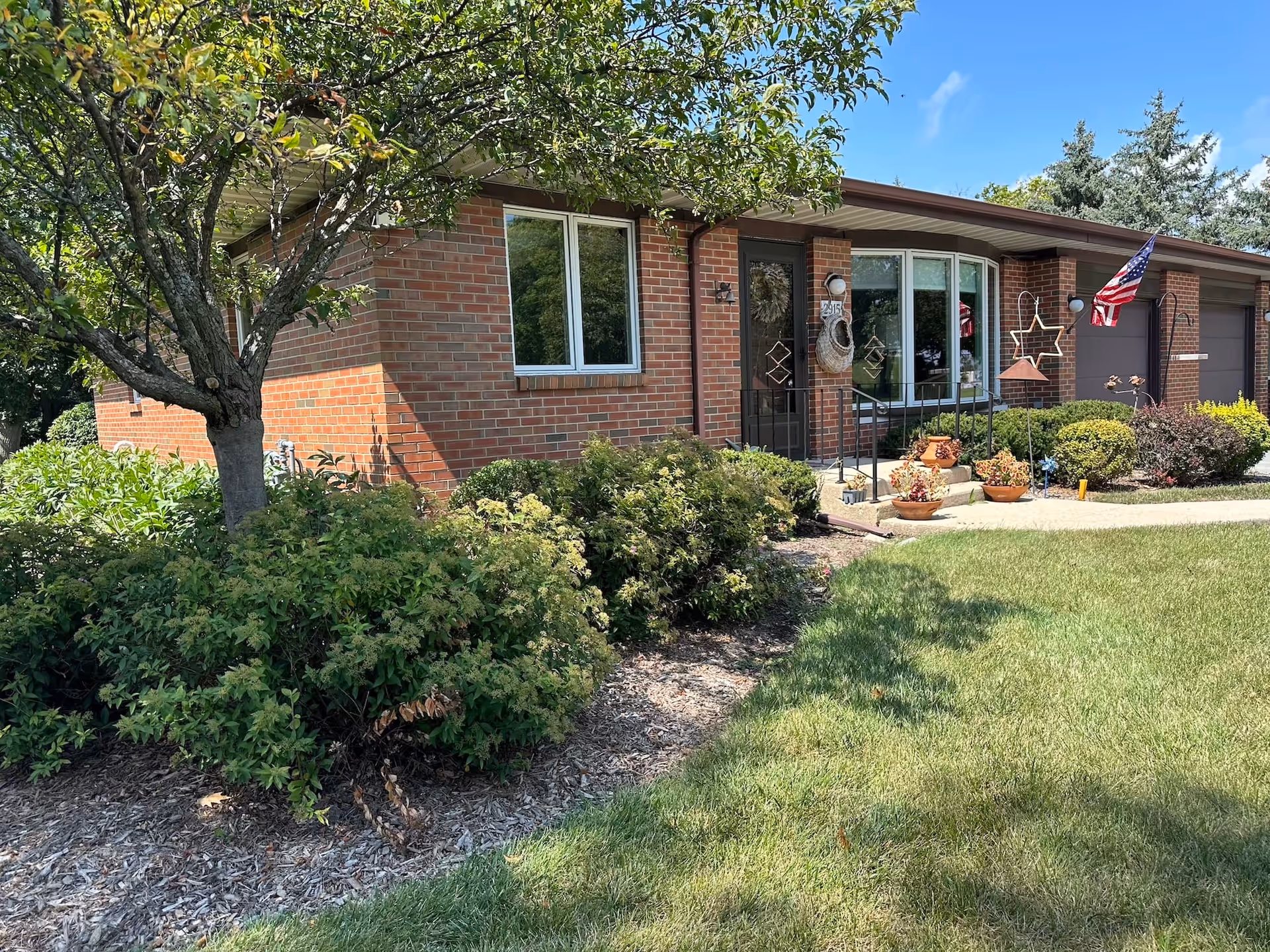 Front exterior of a single-story brick home with a small porch, shrubs, and an American flag.
