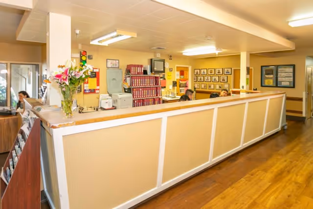 Long reception desk in a senior living facility lobby with staff working behind the counter, flowers on the counter, and file folders on shelves.
