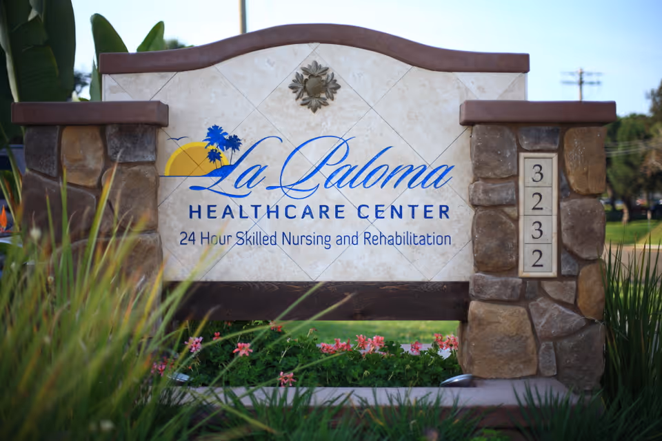 Ornamental stone sign for La Paloma Healthcare Center displaying the facility name, '24 Hour Skilled Nursing and Rehabilitation', address numbers 3232, and surrounding landscaping.