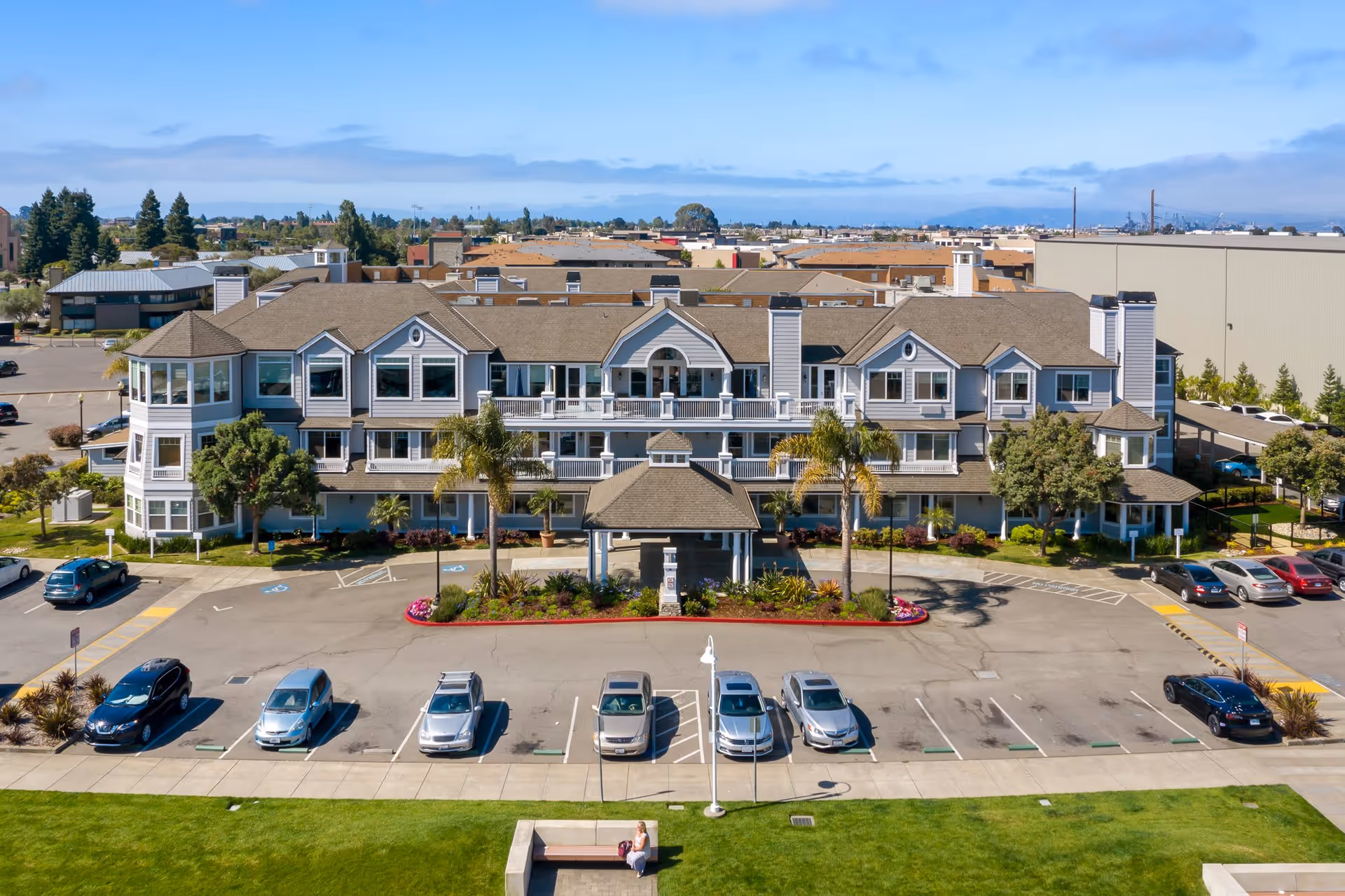 Front exterior view of a large, multi-story senior living facility named Cardinal Point with a parking lot in front, several parked cars, landscaped greenery, and a clear blue sky.