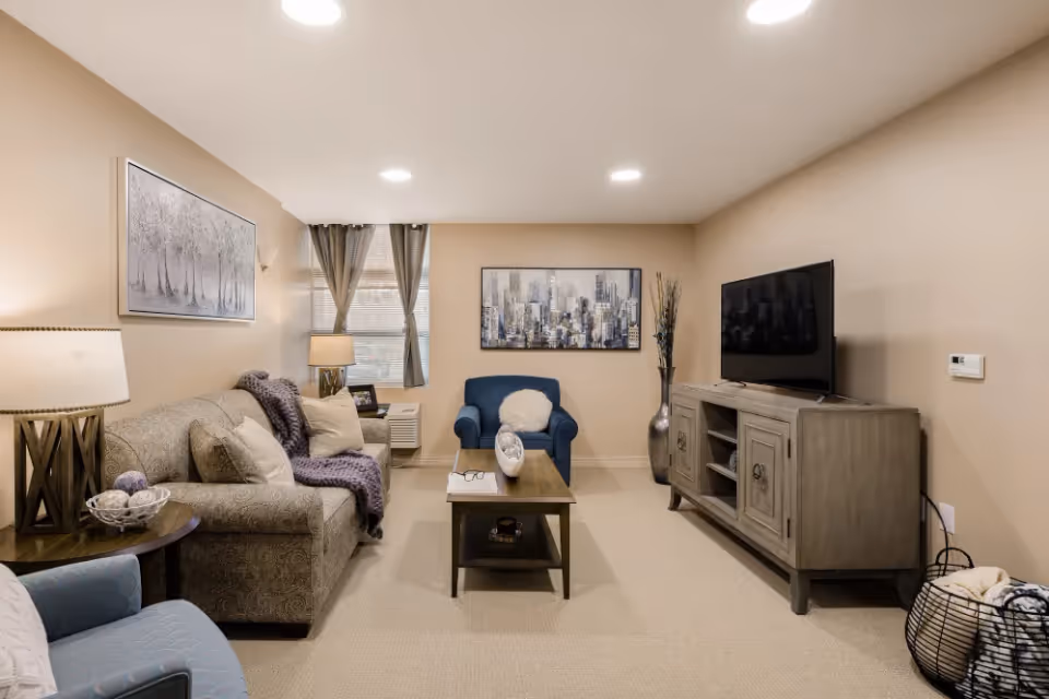 Cozy living room with a sofa, armchairs, coffee table, TV on a console and wall art.