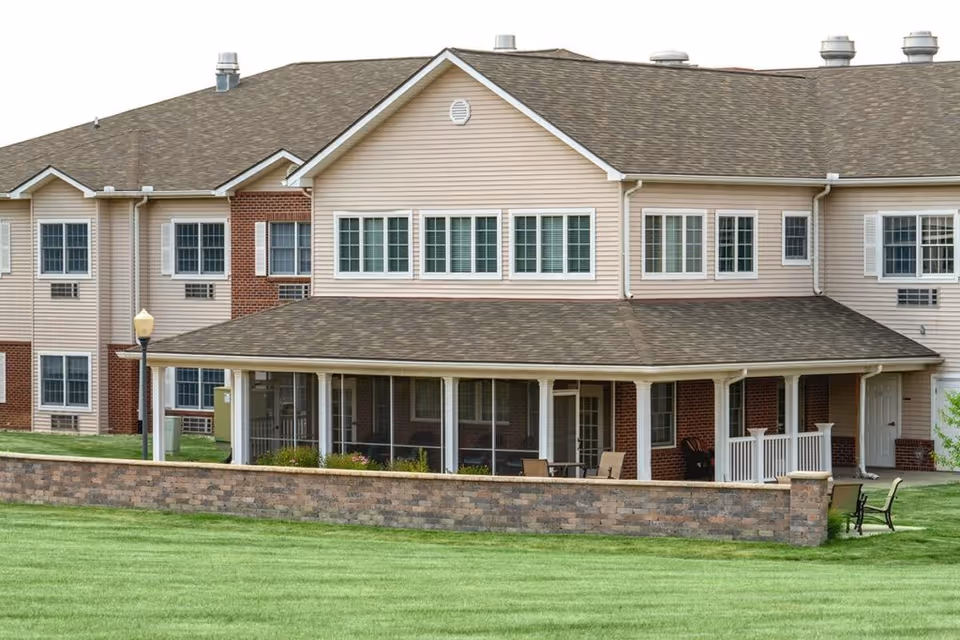 Front exterior of a two-story senior living building with a covered porch, brick accent wall, and manicured lawn.