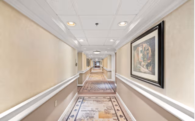 Well-lit interior hallway with patterned runner carpets, handrails and framed artwork along the walls.