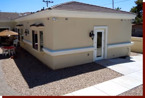 Single-story beige building exterior with gravel yard and outdoor seating under an umbrella.