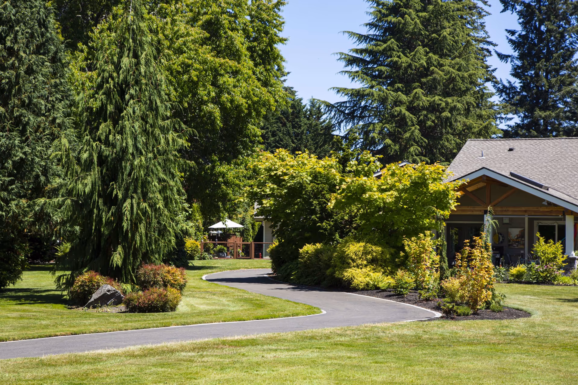 A paved winding path through manicured lawns and trees leading to a single-story building with a covered porch.