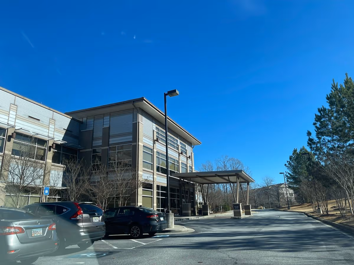 Entrance and driveway of a modern senior living facility building with parked cars under a clear blue sky.