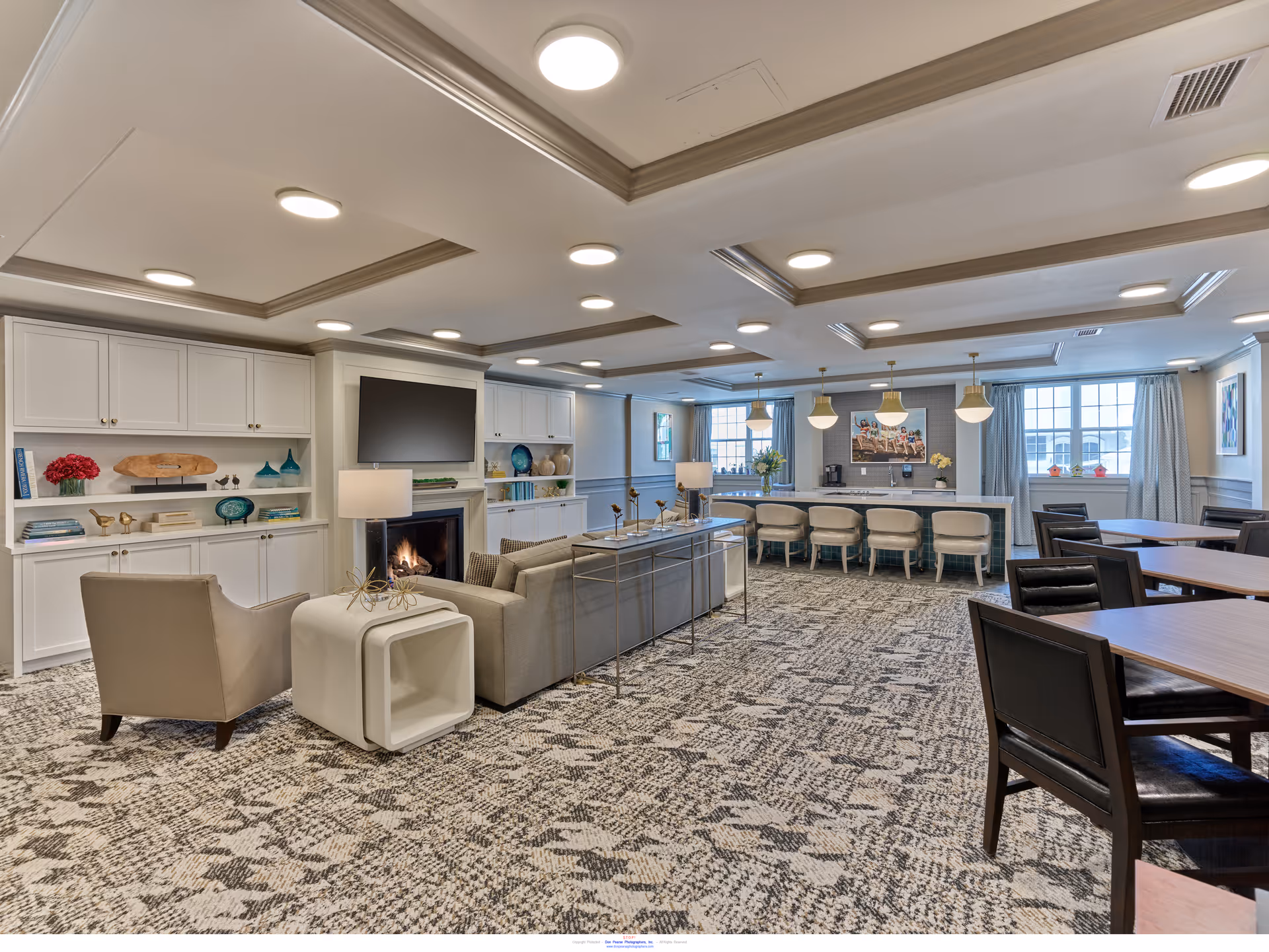 Spacious senior living common area with seating around a fireplace, a bar counter with stools, and dining tables.
