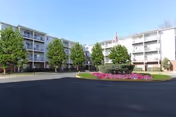Exterior view of a multi-story senior living complex with a circular flower bed and trees.