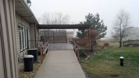 Exterior view of Dolphin Manor showing a concrete walkway, ramp, and grassy yard.