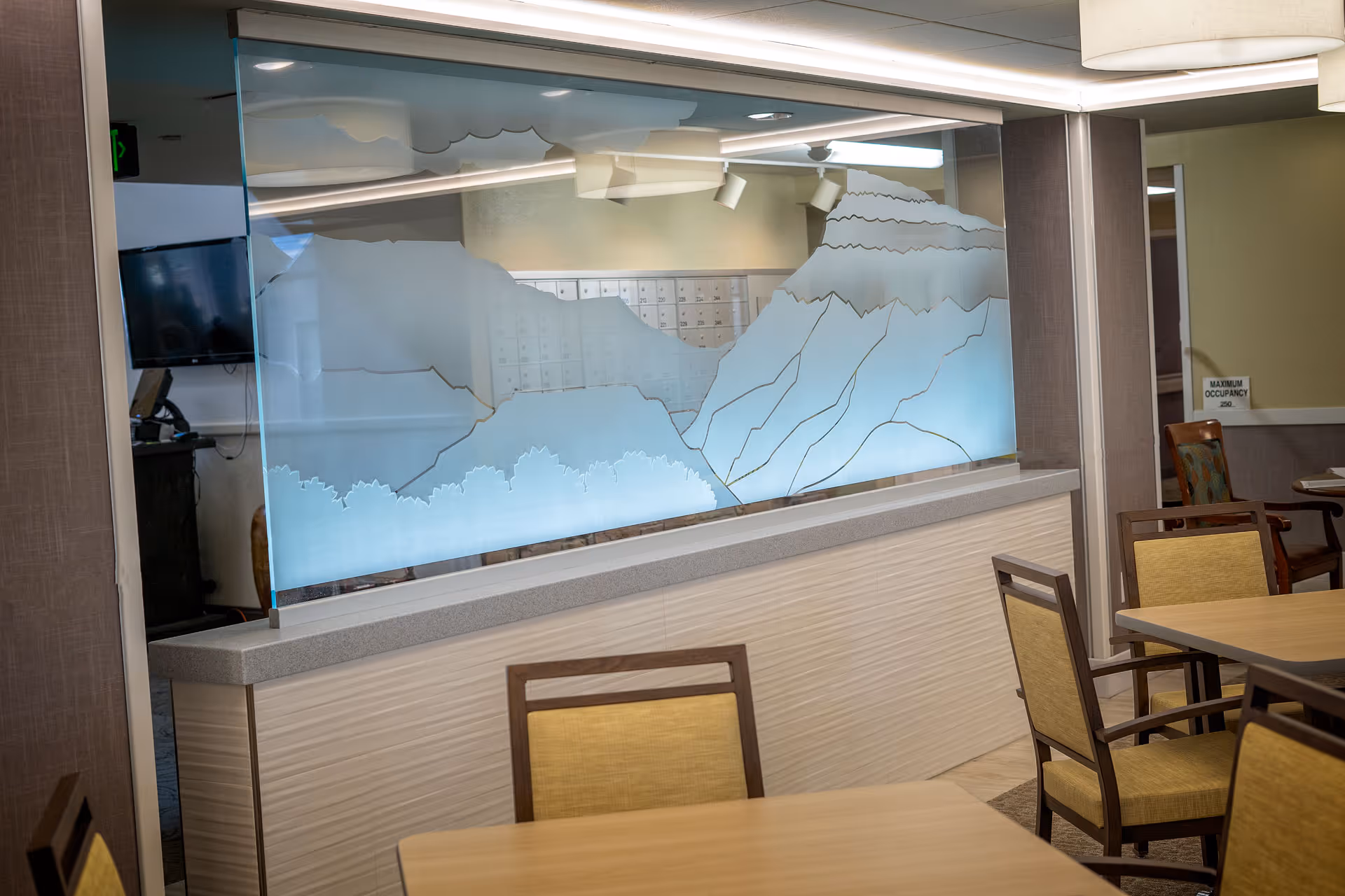 Dining room with tables and chairs and a decorative frosted glass partition etched with a mountain landscape.
