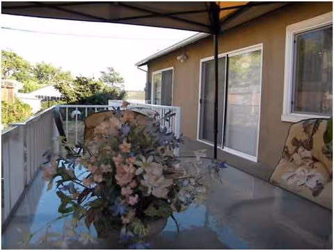 Outdoor balcony patio with a floral centerpiece on a glass table and chairs.