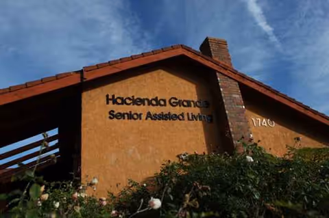 Front exterior of Hacienda Grande Senior Assisted Living with a sign on orange stucco wall.