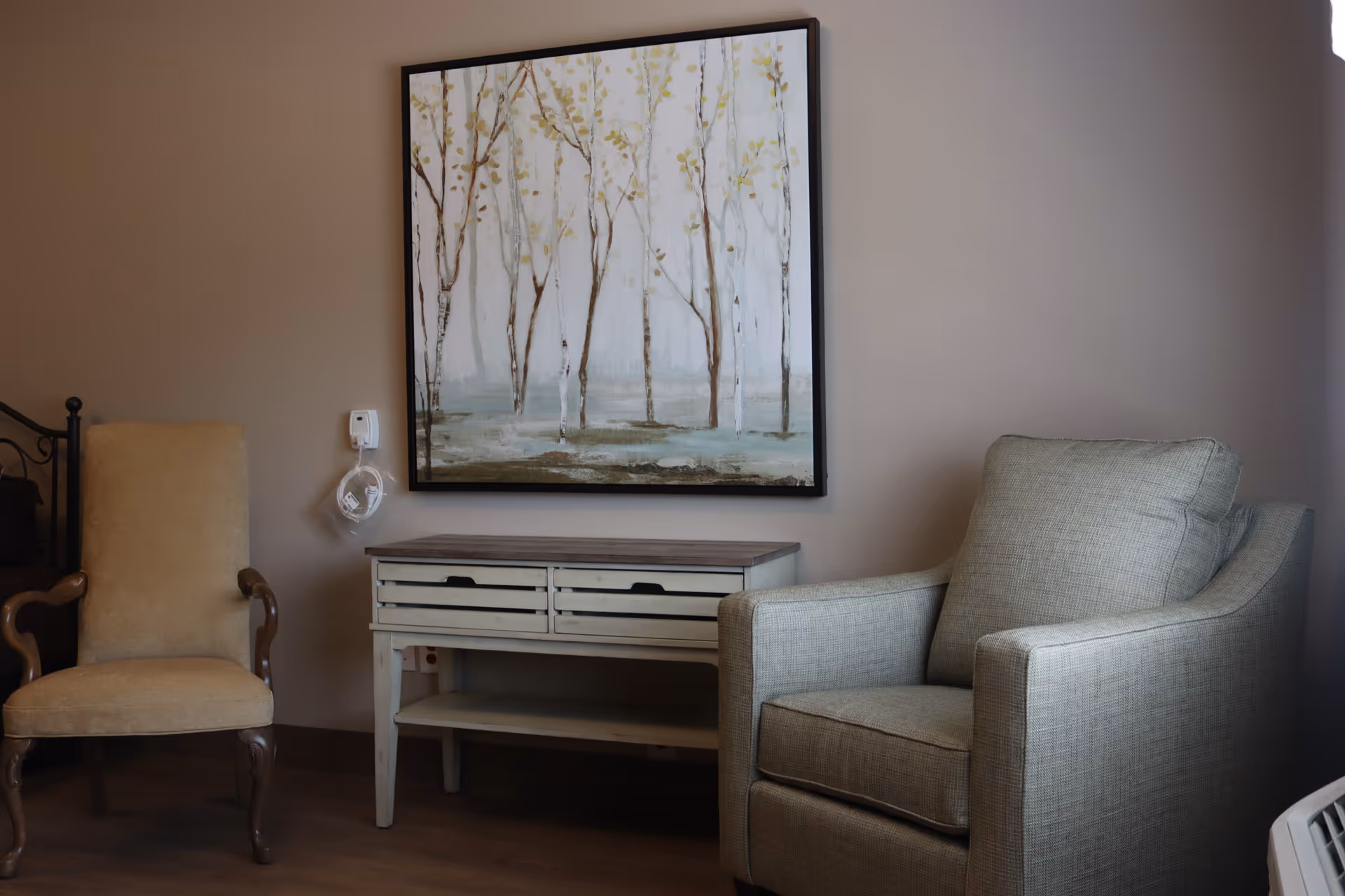 Cozy sitting area with two armchairs, a small console table, and a framed tree painting on the wall.