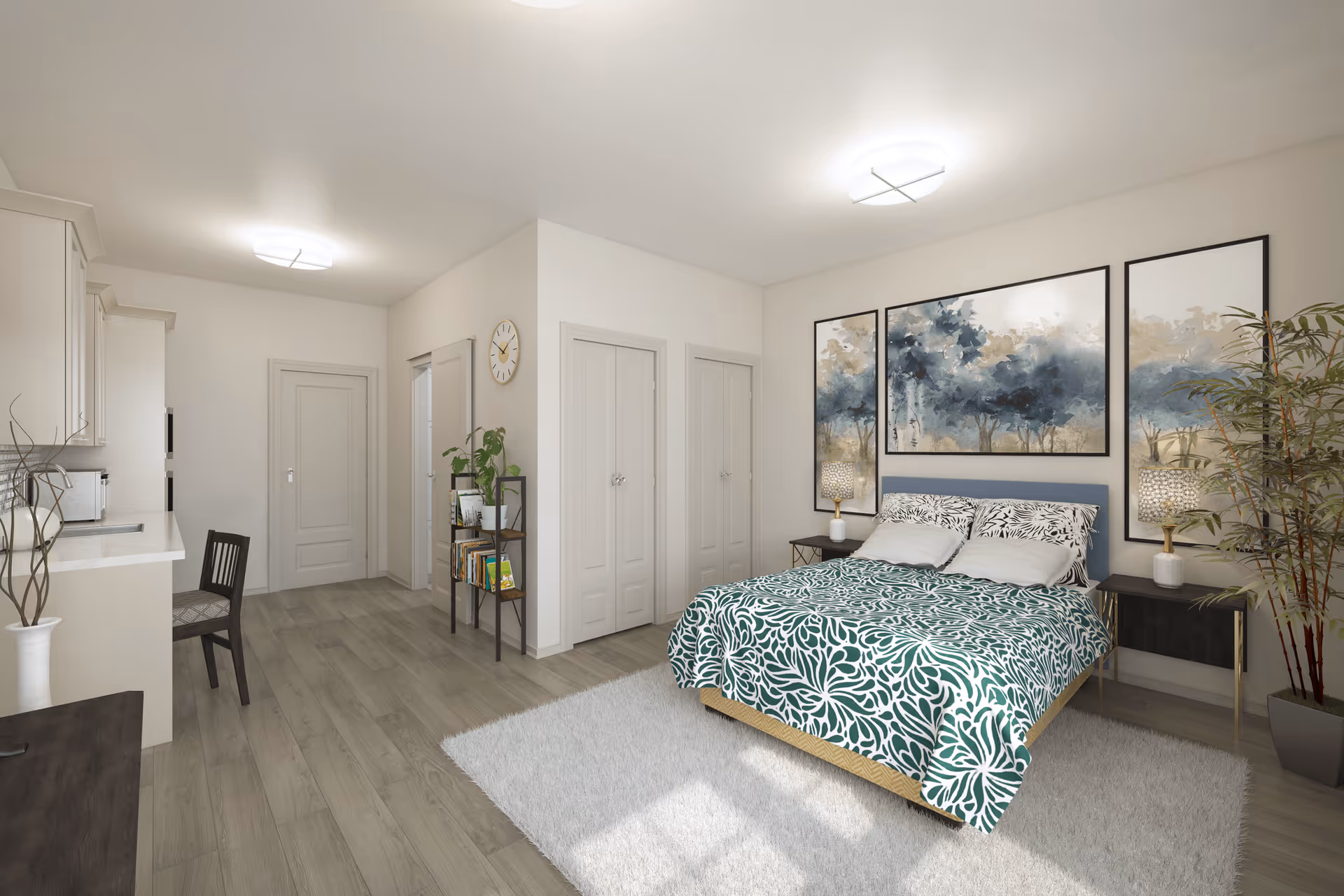 A bright, modern bedroom with a bed covered in a green and white patterned bedspread, two bedside tables with lamps, and three large framed artworks of trees on the wall behind the bed. The room has light wood flooring, a white rug, a tall potted plant, a small bookshelf with plants and books, and a kitchen area with a chair and countertop visible to the left.