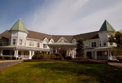 A large senior living facility with green-topped towers, central entrance, and manicured lawn.
