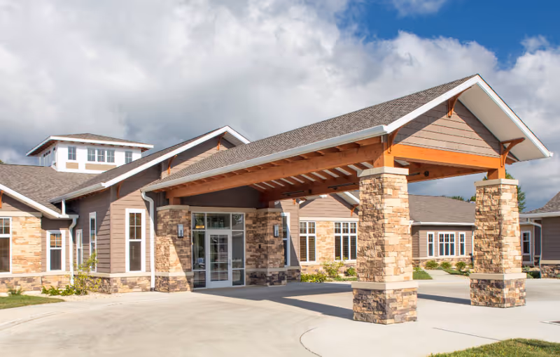 Exterior view of Grand Meadows Senior Living entrance with a covered porte-cochère and stone pillars.