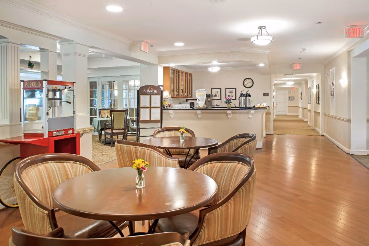 Bright communal dining area with round tables and striped chairs, a popcorn machine, and a service counter in the background.