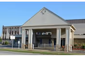 Front exterior view of Cardinal Nursing and Rehabilitation building with a covered entrance supported by columns and a clear blue sky in the background.