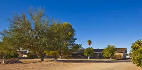 Exterior view of a low, single-story building surrounded by trees under a blue sky.